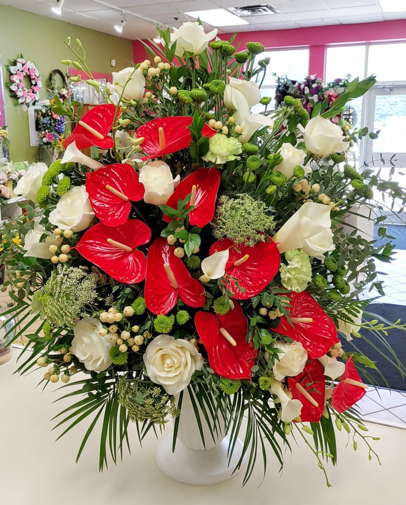 Tribute flower arrangement with red anthiriums, white roses and white snapdragons.