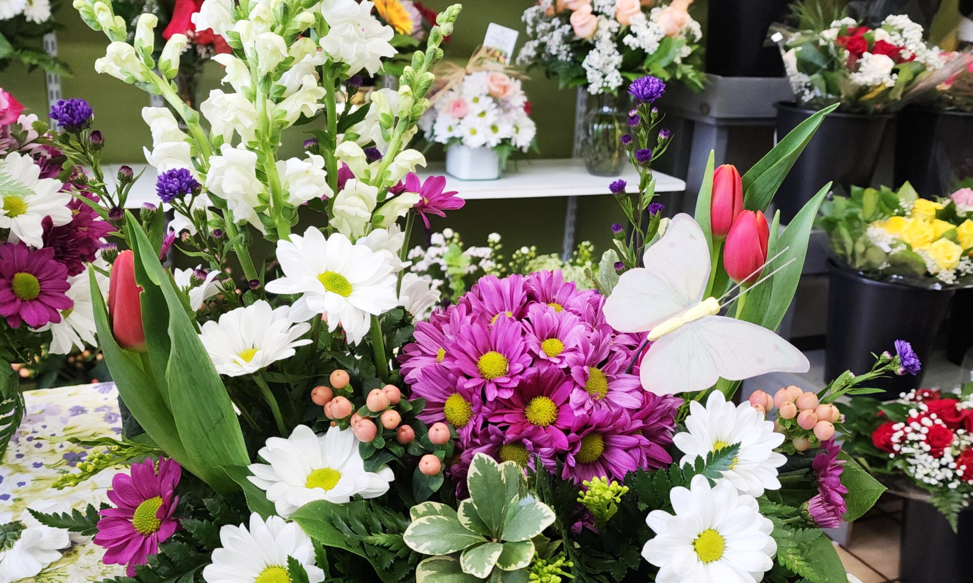 Vibrant spring flower arrangement with white daisies, pink mums, red tulips and fresh greenery on display inside a local Brantford flower shop.